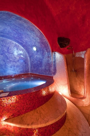 Un jacuzzi con detalles de mosaico rojo, una zona de ducha y una encimera de mármol.
