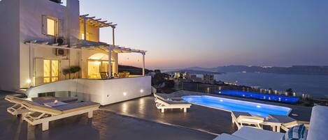 A modern villa with a pool, outdoor seating, and a view of the sea.