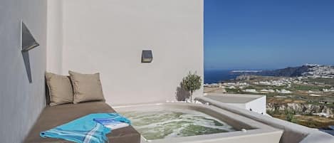 A room with a bed, a small hot tub, and a view of the landscape.