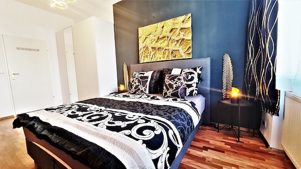 Ein Schlafzimmer mit einem Bett, einem Nachttisch, einem Wandbild und einer Zierpflanze.