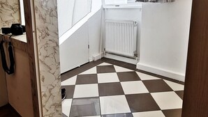 Ein Zimmer mit Schachbrettfußboden, einem Heizkörper, einem Fenster mit durchsichtigen Vorhängen und einer Tür mit Griff.