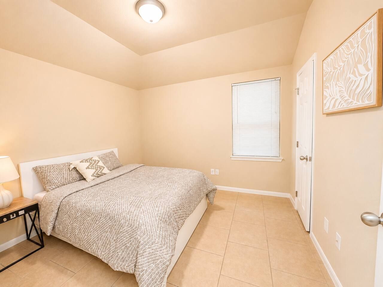 A bedroom with a bed, a nightstand, a window with blinds, and a door.