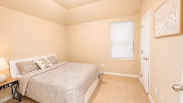 Un dormitorio con cama, mesita de noche, ventana con persianas y puerta.