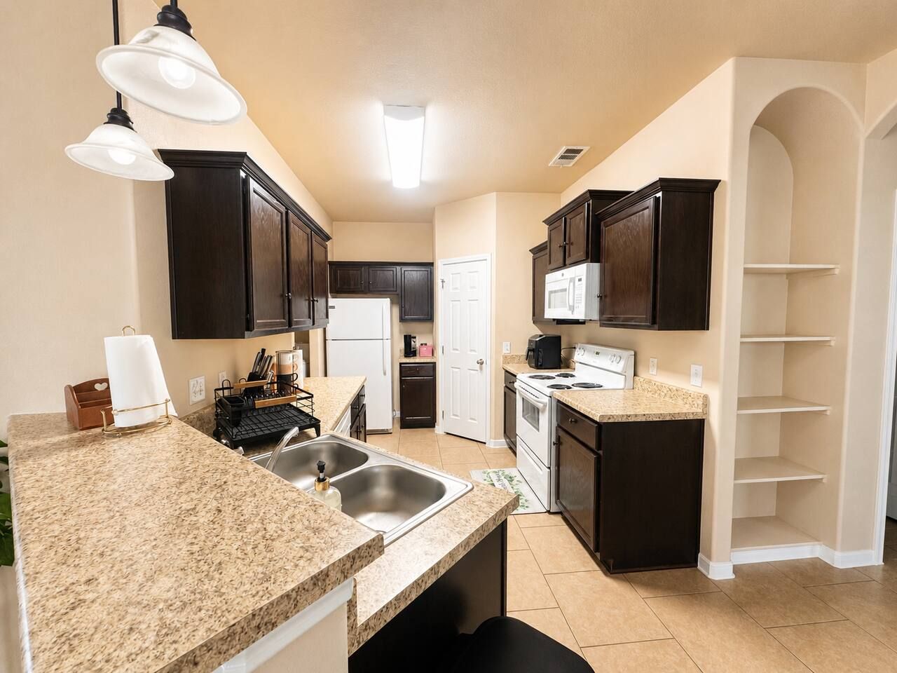 Una cocina con encimeras de granito, muebles oscuros, un lavamanos doble, estufa y microondas.
