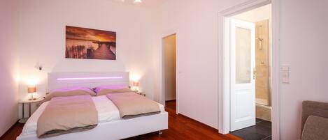 A bedroom with a bed, bedside lamps, a wall-mounted picture, and a door leading to a bathroom.