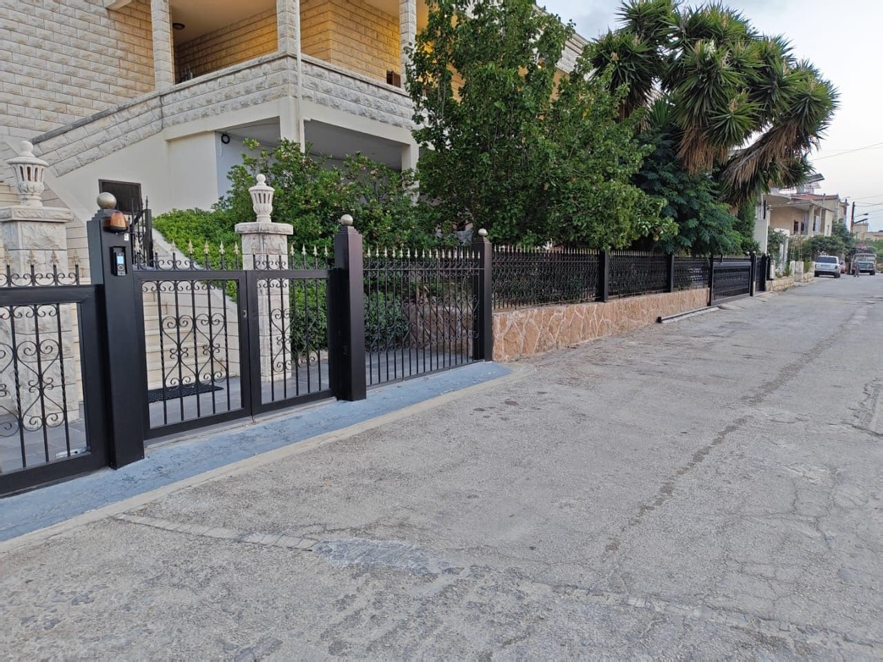 A gated residential area with a paved road, a metal fence, and a building with a balcony.