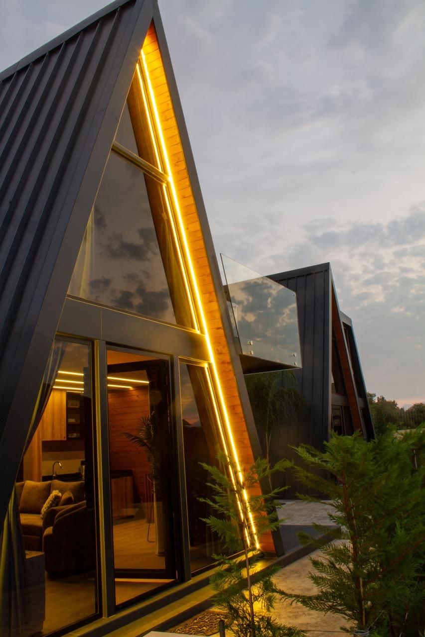 Een modern gebouw met een driehoekig ontwerp, grote glasramen en warme inpandige verlichting.