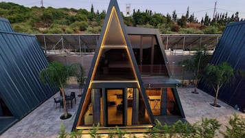 Un edificio moderno de forma triangular con fachada de vidrio, rodeado de vegetación y un área exterior cubierta con asientos.
