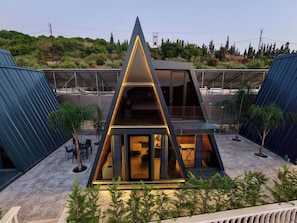 Un edificio moderno de forma triangular con fachada de vidrio, rodeado de vegetación y un área exterior cubierta con asientos.