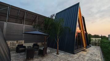 Un patio exterior moderno con zona de comedor, pared de piedra y una estructura arquitectónica distintiva con elementos de vidrio y metal.