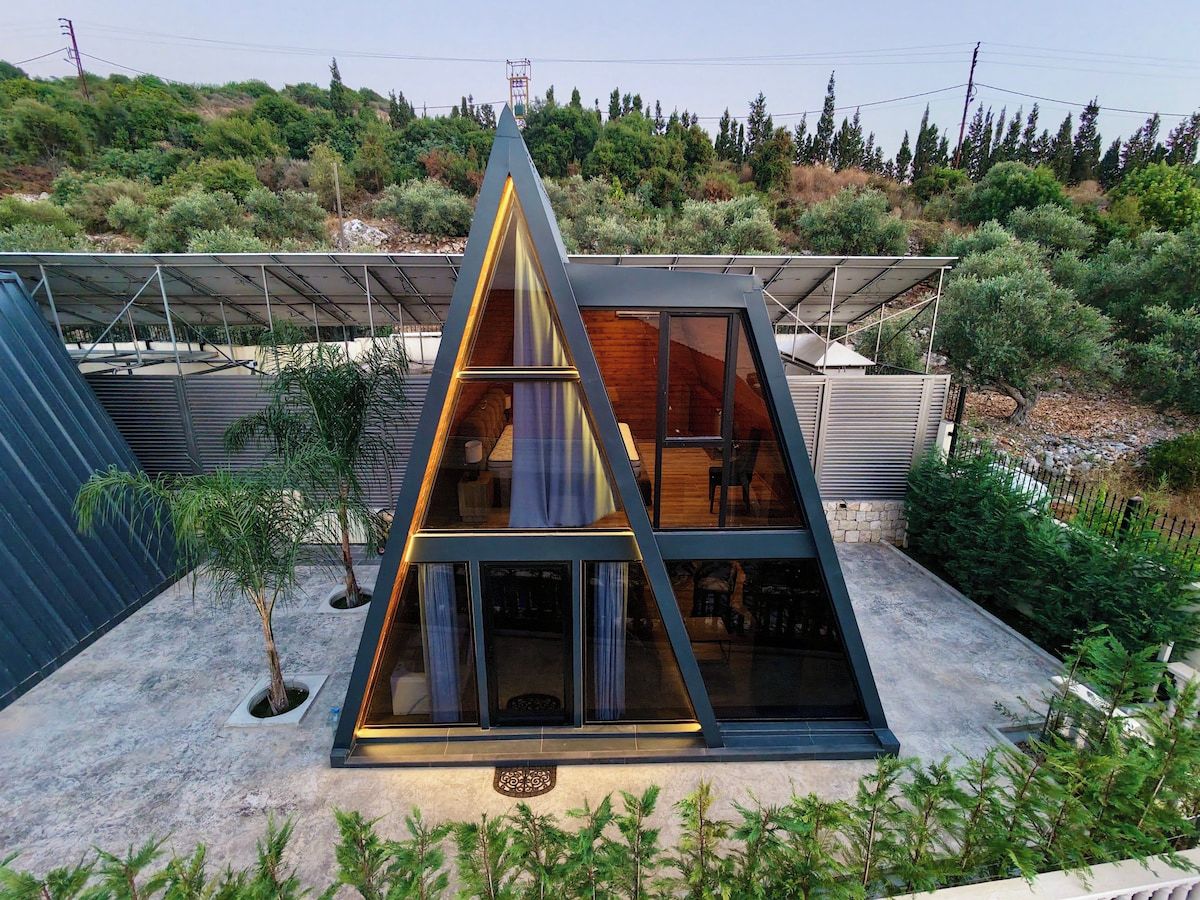 Un edificio moderno de forma triangular con techo plano, ventanas amplias y un área exterior cubierta con paneles solares.