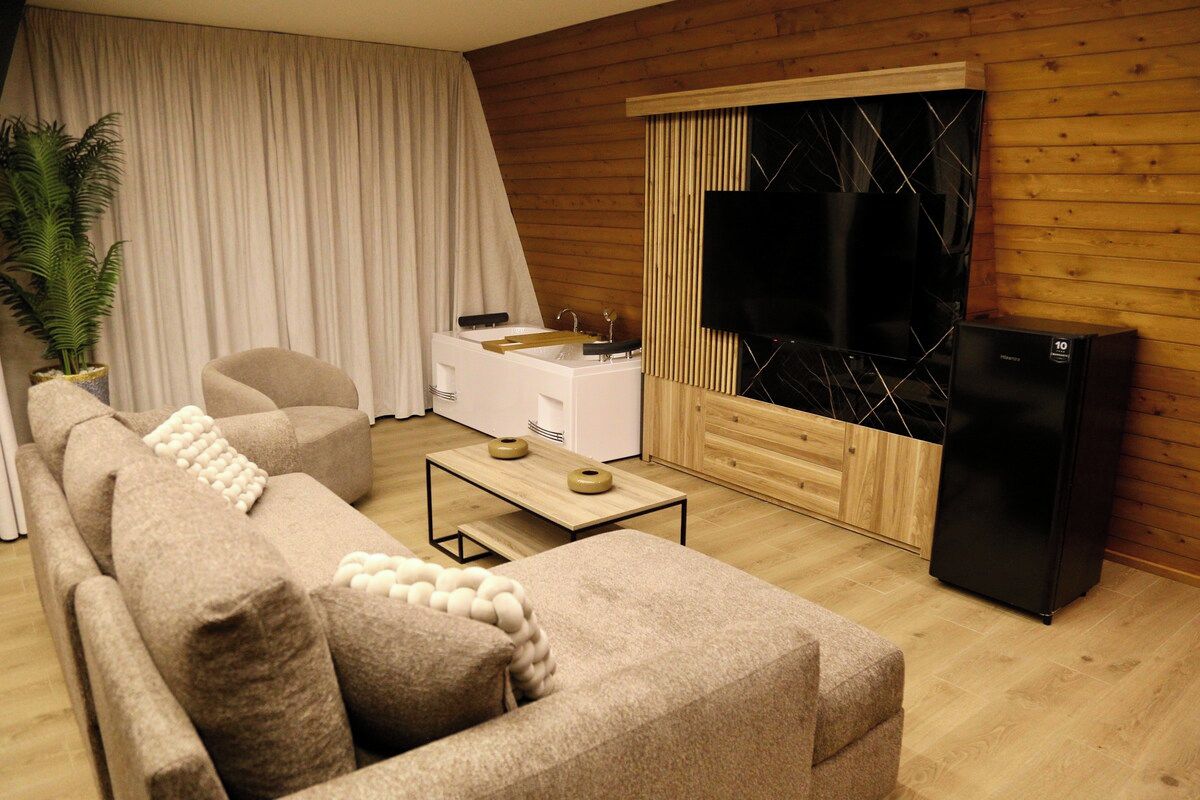 A living room with a sofa, coffee table, TV, and a refrigerator.