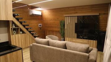 A modern living space with a sofa, wooden walls, a staircase, and a television.