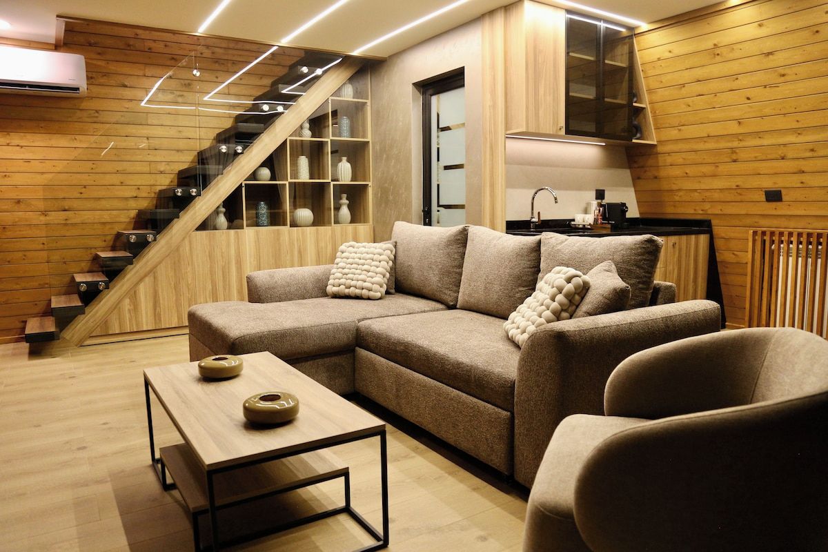 A modern living room with a sectional sofa, a coffee table, and a staircase with built-in shelving.