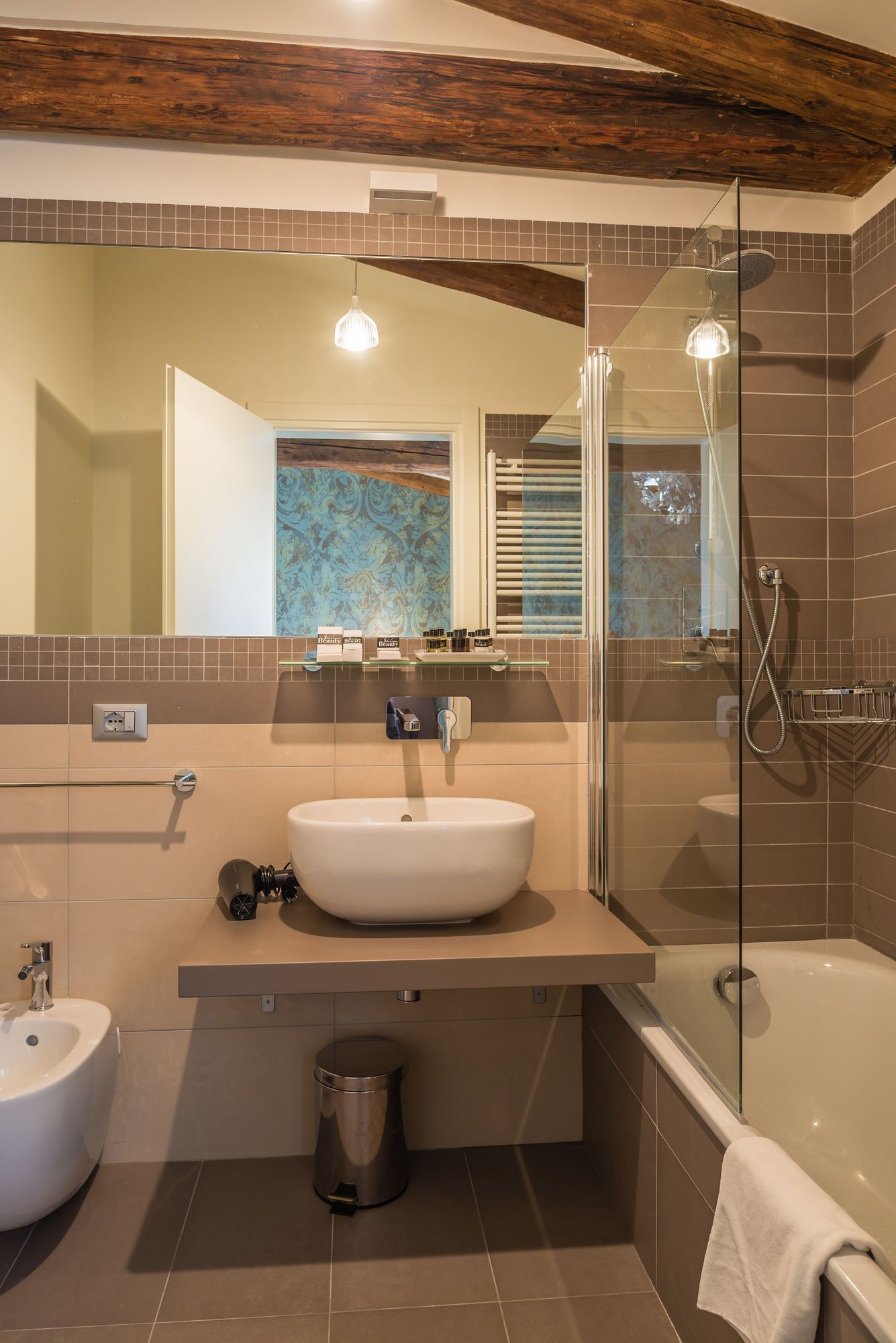A modern bathroom with a large mirror, a sink, a bidet, and a glass-enclosed shower.