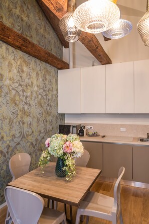 A modern kitchen with white cabinets, a wooden dining table, and a vase of flowers. - Polo's Treasures (Venice)