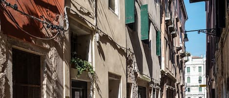 Una calle estrecha bordeada por edificios de varios pisos, algunos con balcones y plantas en macetas.