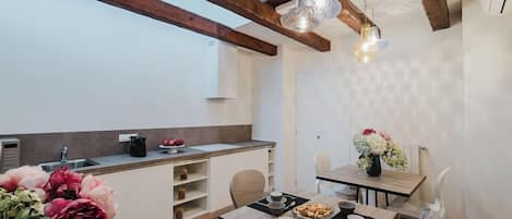 Una cocina moderna con vigas de madera, un comedor con mesa dispuesta para dos personas, y un ventanal que proporciona luz natural.