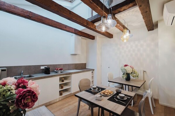 Una cocina moderna con vigas de madera, un comedor con mesa dispuesta para dos personas, y un ventanal que proporciona luz natural.