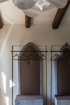 A room with a wooden ceiling, two arched niches with hanging clothes, and a bench. - Polo's Treasures (Venice)