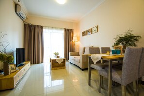 A modern living room with a sofa, a dining table with chairs, a flat-screen TV, and a potted plant. - Xizhengjia Hotel Apartment Pazhou Complex (Guangzhou)