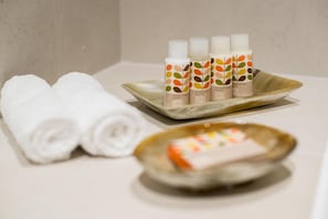 Un baño con toallas blancas ordenadas, una bandeja con cuatro botellas de loción corporal y un recipiente con una pastilla de jabón.