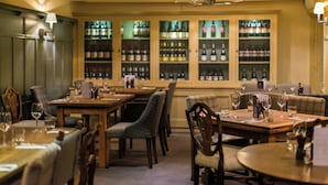 Interior de restaurante con mesas dispuestas para comer, sillas y una cava de vinos al fondo.