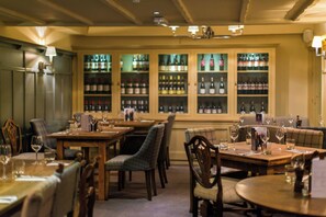 A restaurant interior with tables set for dining, chairs, and a wine rack in the background.