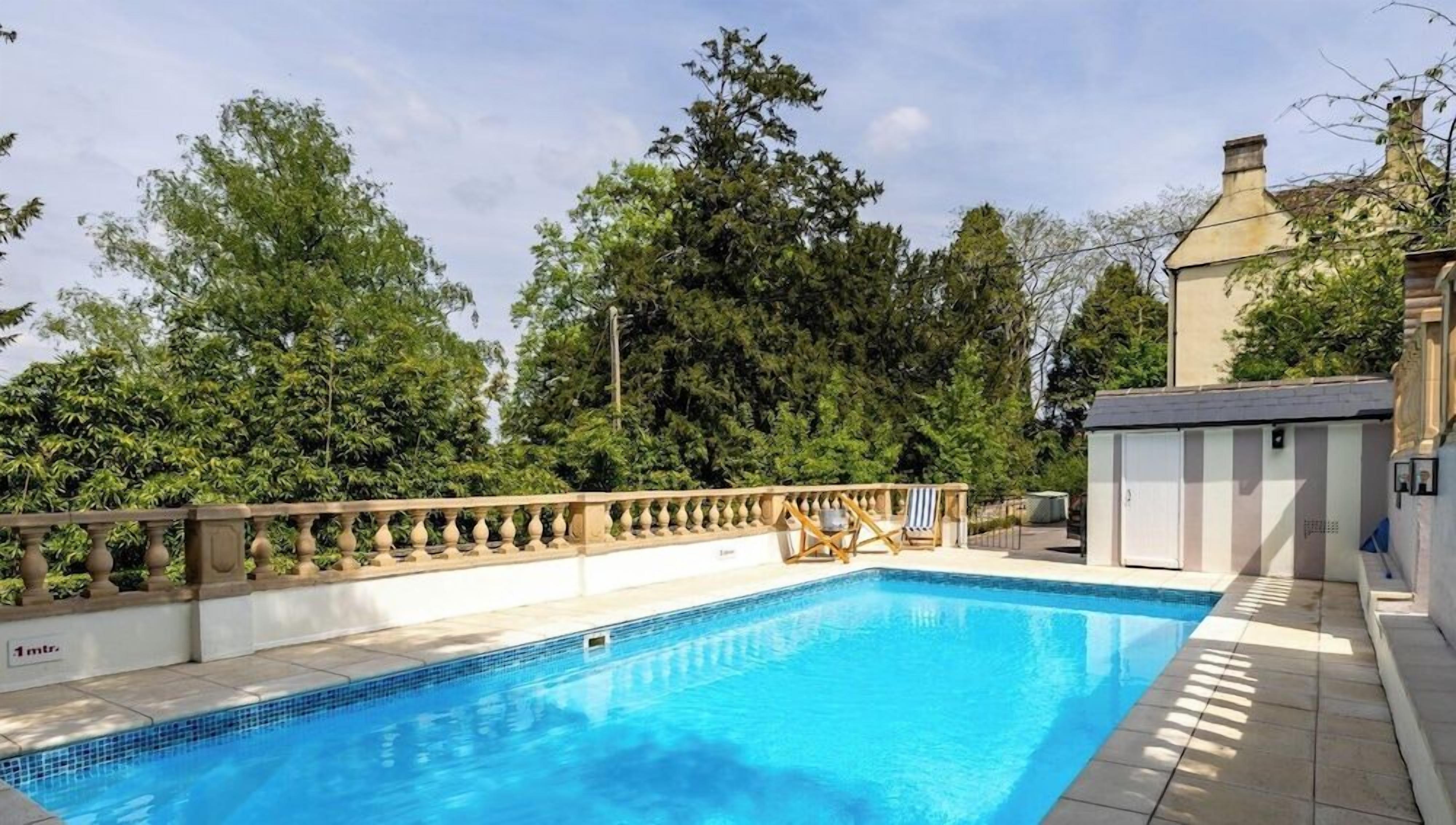 A rectangular swimming pool with a tiled edge, surrounded by a wooden deck and a low stone wall.