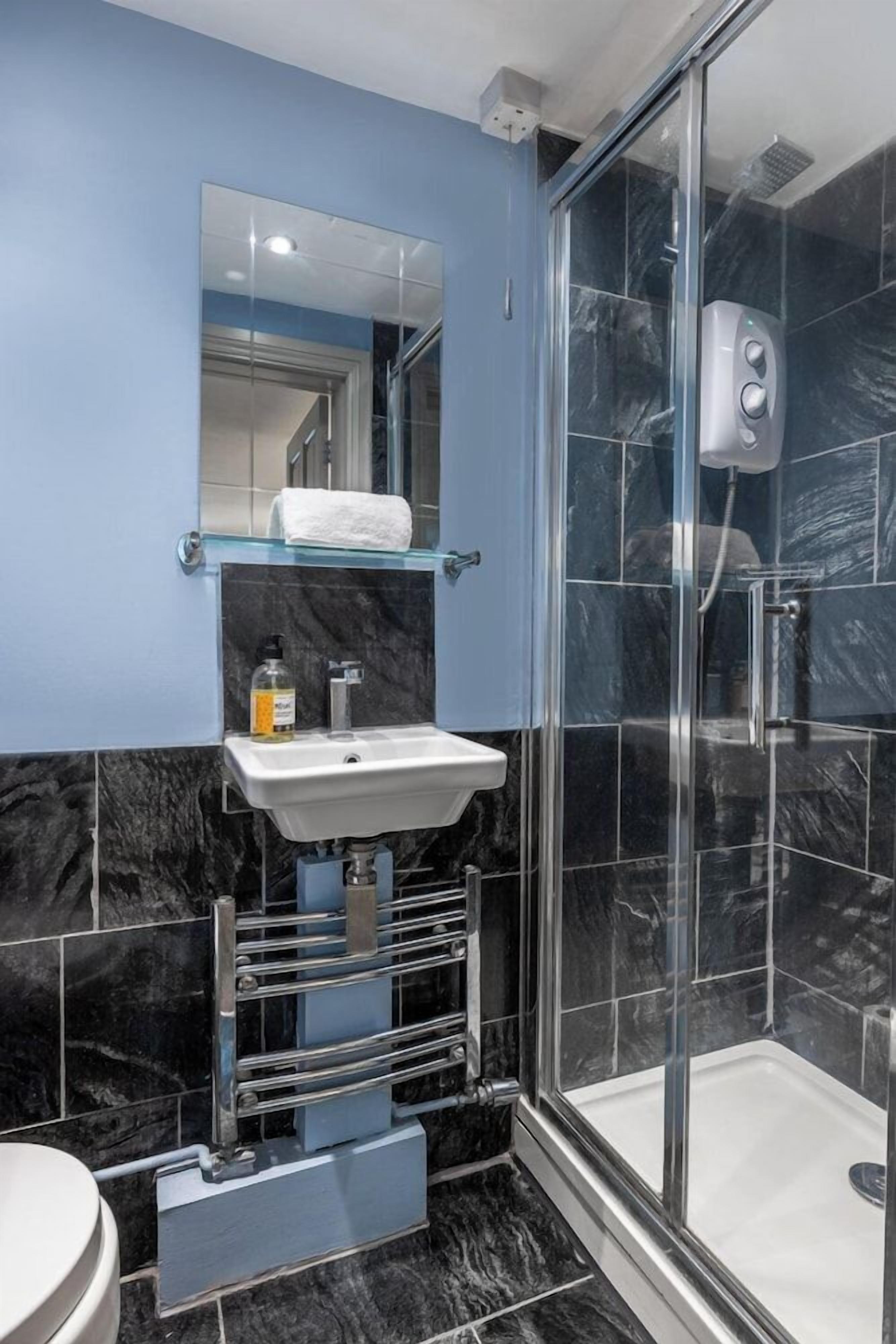 A bathroom with a glass shower enclosure, a white sink, and a marble-tiled wall.