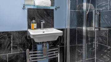 A bathroom with a glass shower enclosure, a white sink, and a marble-tiled wall.