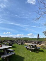 Un área de estar al aire libre con varias mesas de picnic y una única sombrilla.