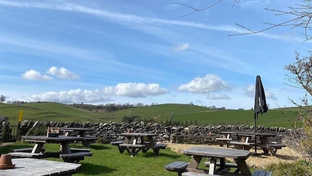 An outdoor seating area with multiple picnic tables and umbrellas, set against a backdrop of green hills and a clear sky. - Nateby Inn (Kirkby Stephen)