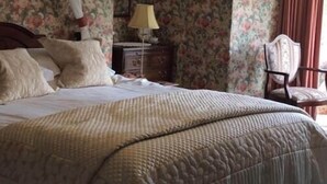 Een slaapkamer met een groot bed, een nachtkastje, een stoel en bloemenbehang.