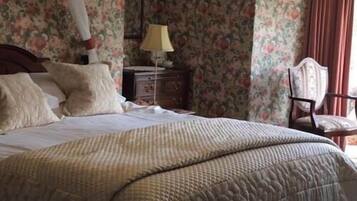 Una cama con cubrecama acolchado, una mesita de noche con lámpara y una silla en una habitación con papel tapiz floral.