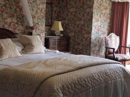 A bedroom with a large bed, a nightstand, a chair, and floral wallpaper.