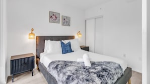A modern bedroom with a large bed, two bedside tables, and wall-mounted lamps. - Downtown Suites Near Eaton Centre (Toronto)