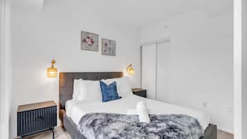 A modern bedroom with a large bed, two bedside tables, and wall-mounted lamps.