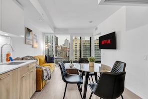 A modern apartment with a kitchen, dining area, and a large window offering a city view. - Downtown Suites Near Eaton Centre (Toronto)