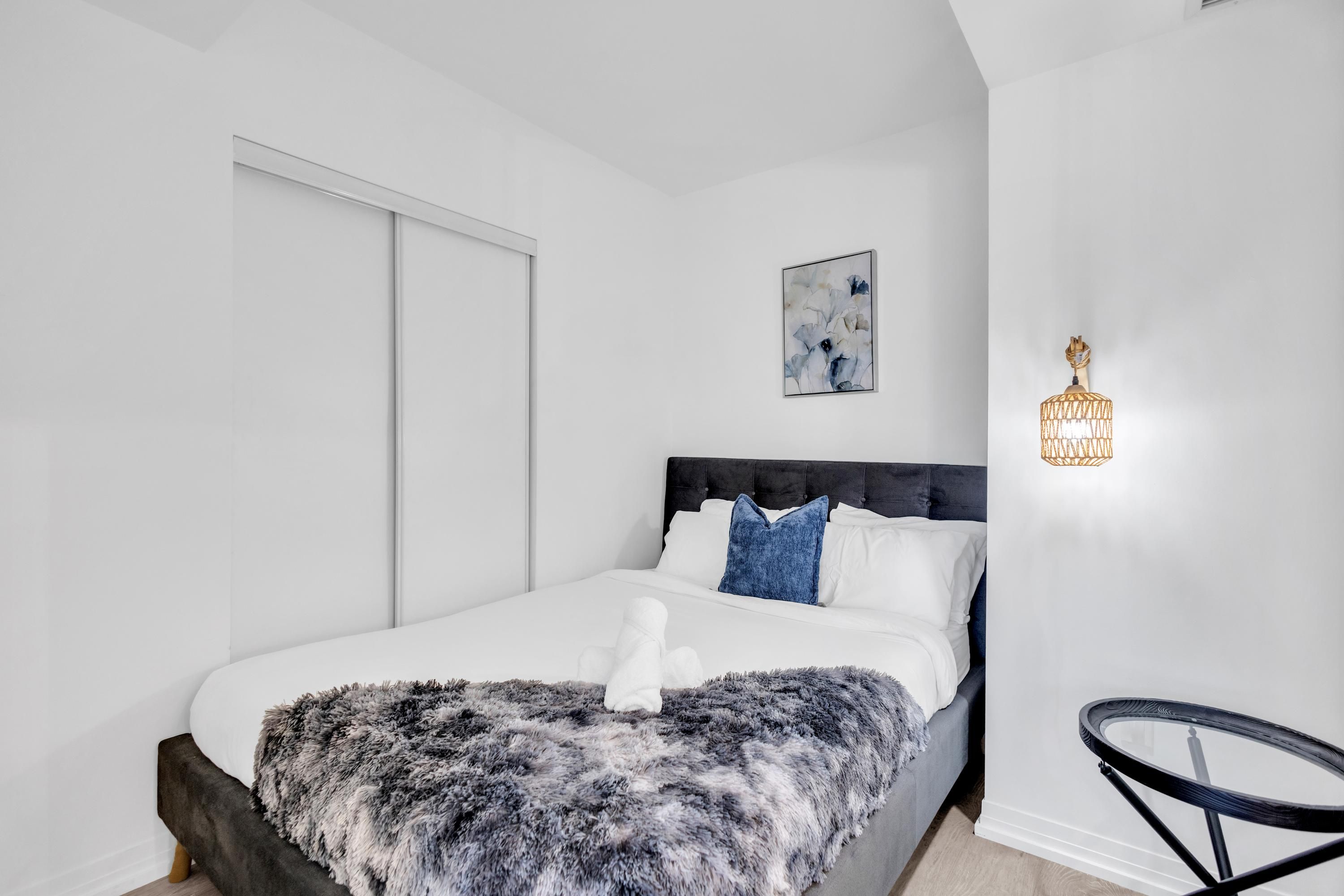 A modern bedroom with a large bed, a fluffy blanket, and a unique wall-mounted light fixture.