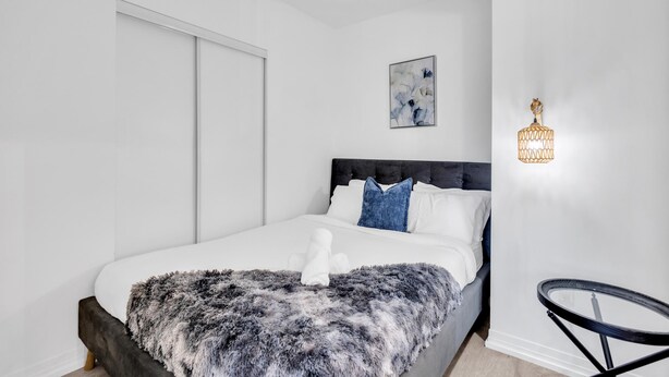 A modern bedroom with a large bed, a fluffy blanket, and a unique wall-mounted light fixture. - Downtown Suites Near Eaton Centre (Toronto)