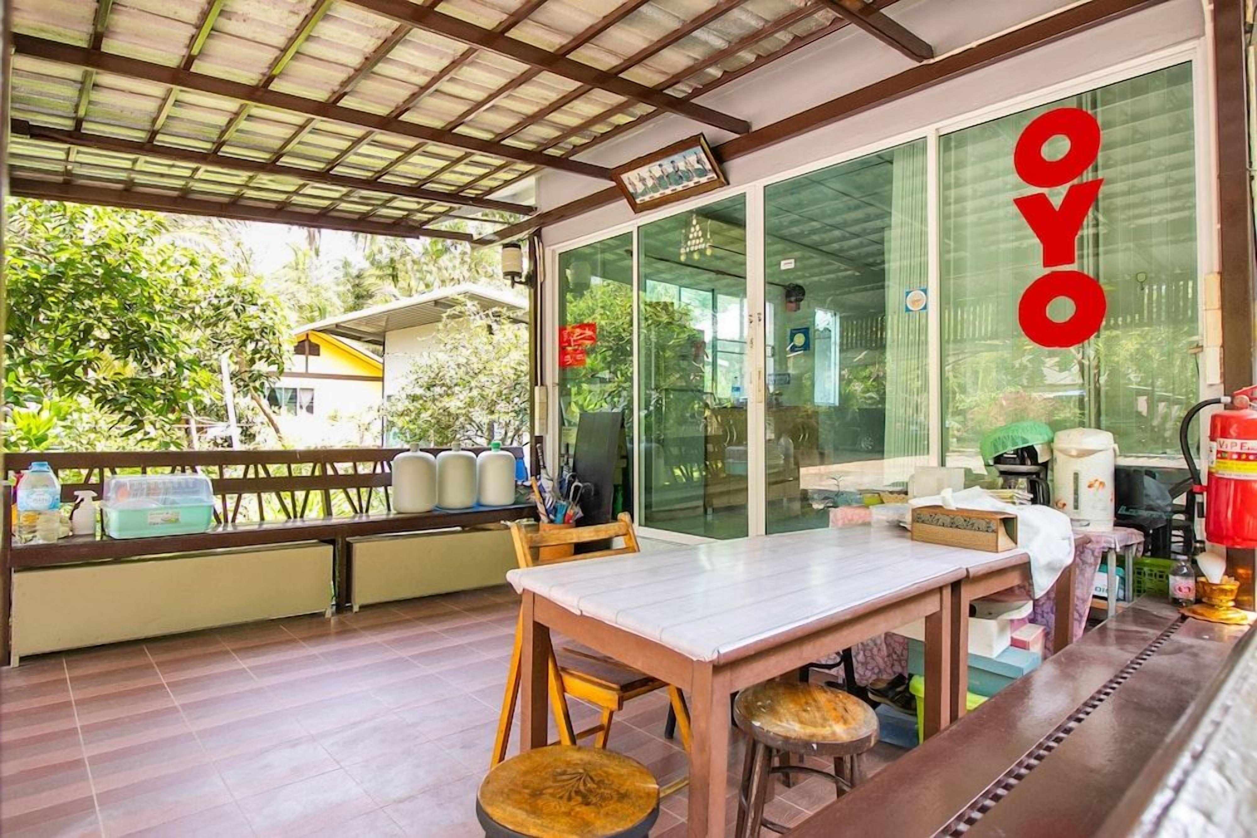 A covered outdoor seating area with a table and chairs, a bench, and a view of the surrounding greenery.