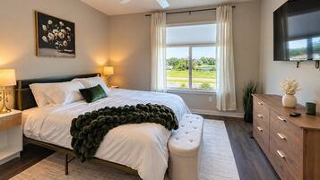 A bedroom with a bed, a ceiling fan, a window with curtains, a television, and a bedside table with a lamp.