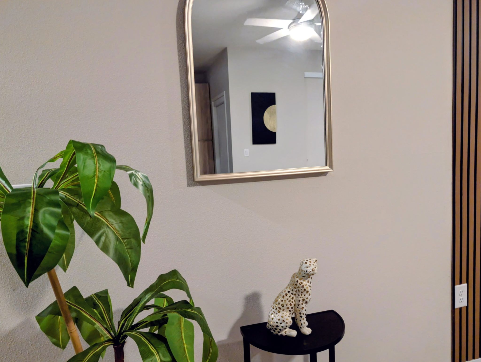 Een kamer met een grote spiegel, een kamerplant en een luipaardbeeldje op een bijzettafeltje.