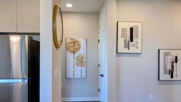 A modern kitchen with a stainless steel refrigerator, a hallway with a door, and two framed artworks on the wall.