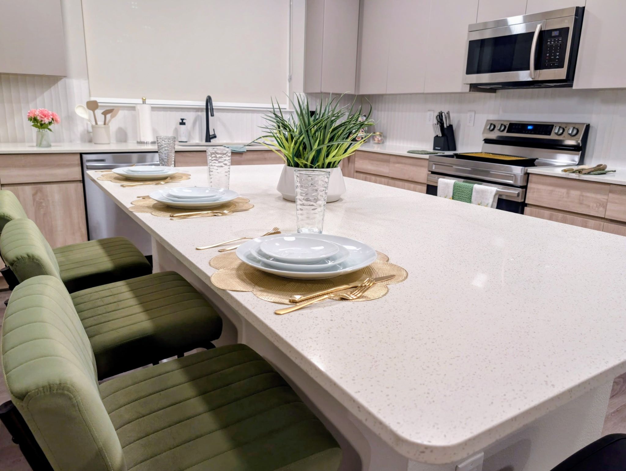 A modern kitchen with a central island, stainless steel appliances, and green upholstered bar stools.
