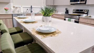 A modern kitchen with a central island, stainless steel appliances, and green upholstered bar stools.