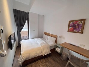 Habitación de hotel con cama, escritorio, silla, televisor y ventana con cortinas.