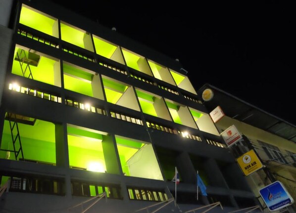 En bygning med flere etager, oplyste vinduer og skilte, der angiver faciliteter som NOK Air og en swimmingpool.