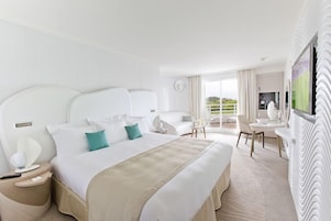 A hotel room with a large bed, a desk, a chair, and a balcony with a view.